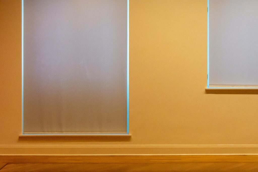 A minimalist beige wall with two covered window blinds, offering a serene indoor atmosphere.